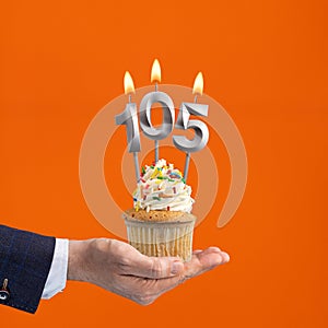 The hand that delivers cupcake with the number 105 candle - Birthday on orange background