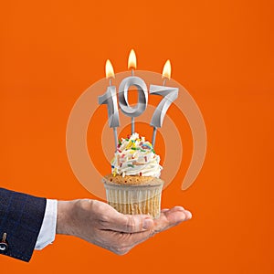 The hand that delivers cupcake with the number 107 candle - Birthday on orange background