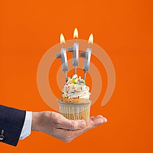 The hand that delivers cupcake with the number 111 candle - Birthday on orange background