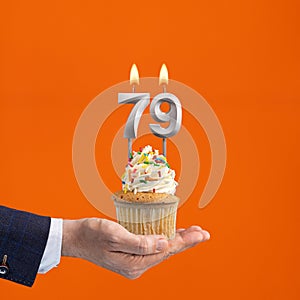 The hand that delivers cupcake with the number 79 candle - Birthday on orange background