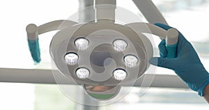 the hand of a dentist doctor turns on the lamp of the dental chair in his office against the background of a window