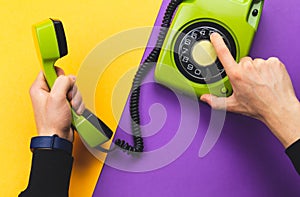 Hand dialing a number on a classic phone with round dial. vintage green telephone with handset on color background. old