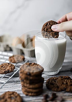 a hand dipping cookie in a tall glass of milk with a stack of homemade chocolate chip cookies