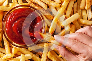 Hand dipping french fries in tomato sauce or ketchup