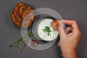 Hand dipping spicy sweet potato chips into yogurt garlic chive dip sauce in black bowls