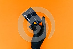 Hand in a disposable black glove with a bank card. Contactless payment of the invoice for purchases by the client during covid-19