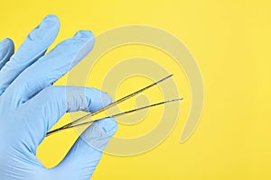 Hand of doctor in blue medical glove holding a tweezers isolated on yellow background