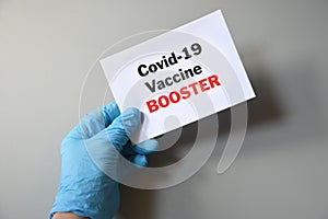 The hand of the doctor hold a white paper with the text `Covid-19 Vaccine Booster`. Concept of Combating the COVID-19 Virus with