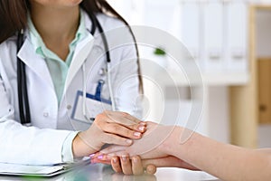 Hand of a doctor woman reassuring to female patient, close-up. Medical ethics and trust concept