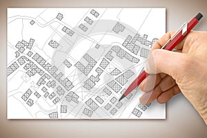 Hand drawing an imaginary catastral map of territory with buildings, fields, roads and land parcel above a desk