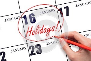 Hand drawing a red circle and writing the text Holidays on the calendar date 16 January. Important date.