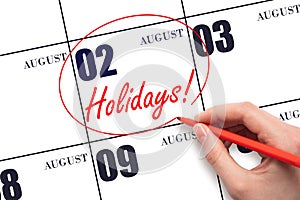 Hand drawing a red circle and writing the text Holidays on the calendar date 2 August. Important date.