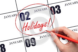 Hand drawing a red circle and writing the text Holidays on the calendar date 2 January. Important date.