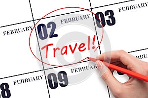 Hand drawing a red circle and writing the text TRAVEL on the calendar date 2 February. Travel planning.