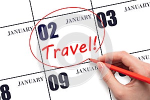 Hand drawing a red circle and writing the text TRAVEL on the calendar date 2 January. Travel planning.