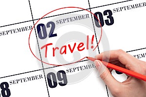 Hand drawing a red circle and writing the text TRAVEL on the calendar date 2 September . Travel planning.