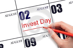 Hand drawing red line and writing the text Invest Day on calendar date August 2. Business and financial concept.