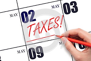 Hand drawing red line and writing the text Taxes on calendar date May 2. Remind date of tax payment