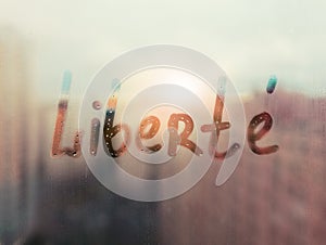 Hand drawn French word Liberte freedom in english on foggy glass on suset window