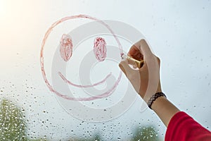 Hand draws a positive smiley on a rainy autumn window