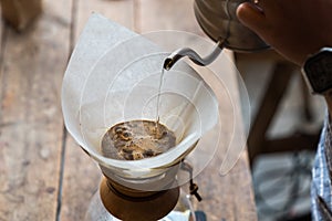 Hand drip coffee, Barista pouring water on coffee ground with filter on wooden table, vintage style