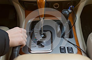 The hand of the driver of the car holding the brake lever, on the background of the automatic transmission controls