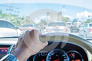 Hand of driver holding steering wheel, with traffic view in the city