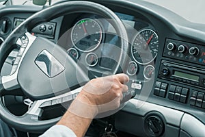 Hand of a driver on steering wheel at intercity coach bus. Focus on steering wheel. Blurry control panel buttons and dials on the