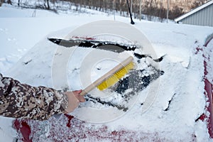 Hand driver using brush sweeping snow on windscreen car