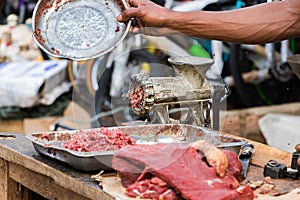 Hand driving away flies over minced meat next to a grinder outdoors in Toliara photo