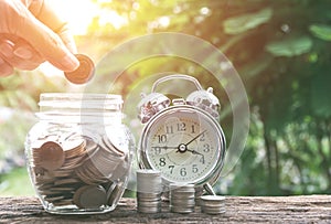 Hand drop a coin in glass jar with money coin stack growing for