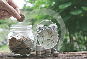 Hand drop a coin in glass jar with money coin stack growing for