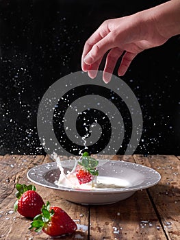 Hand dropping fresh strawberries on a plate with milk