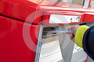 A hand dropping off an envelope into a red post mail box