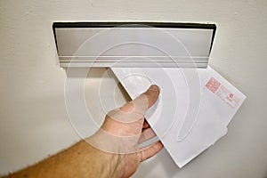 A hand drops an envelope and a parcel into a mailbox,