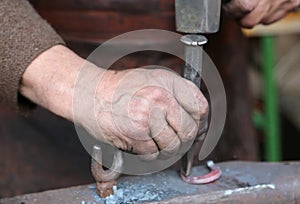 Hand elder blacksmith who uses an iron awl and a hammer over a l