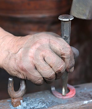 Hand elder blacksmith who uses an iron awl over a anvil