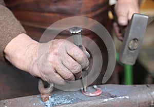 Hand elder blacksmith who uses an iron awl over a large anvil