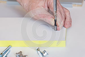 The hand of an elderly man sets the fastener during the assembly of furniture. Close-up. Selective focus