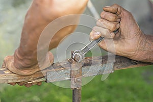 A hand of an elderly man is twisting the nut with a wrench outdoors