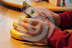 Hand of elderly man uses electronic device resting against bananas