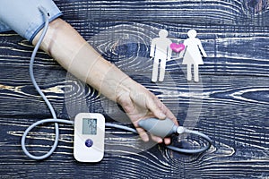 Hand of an elderly person blood pressure monitor. man cut out of paper and red heart on wooden background. Stroke, heart attack