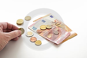 Hand of an elderly woman is counting her money, a few euro coins and banknotes, white background