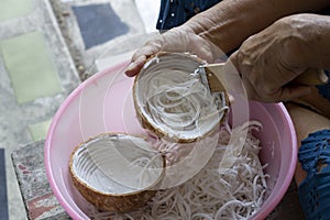 Hand of elderly woman used stainless coconut scraper for shredded coconut meat for make cooking food.