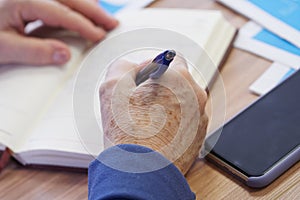 The hand of an elderly woman writing with a fountain pen in a notebook or diary. Memories or a will. Selective focus. No face