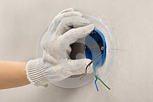 Hand of electrician in glove installing plastic outlet box