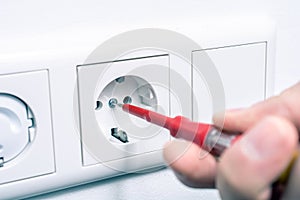 Hand Of An Electrician Using A Phase Tester Screwdriver To Repair A Wall Socket