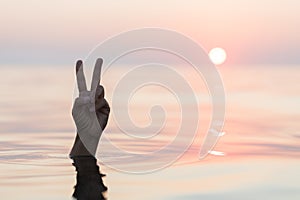 Hand emerging from the sea showing a peace sign