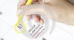 Hand encircles a date on a calendar with text build a great company culture yellow felt-tip pen