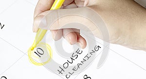 Hand encircles a date on a calendar with text House Cleaning yellow felt-tip pen